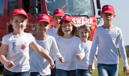 Kinder aus der Kinderfeuerwehr stehen vor einem Feuerwehrfahrzeug