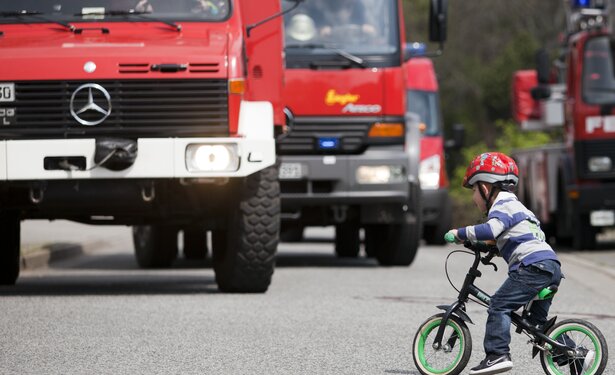 Kind mit Laufrad vor fahrenden Feuerwehrautos