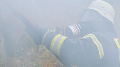Feuerwehrmann mit Schutzkleidung löscht, Rauchgase umhüllen ihn